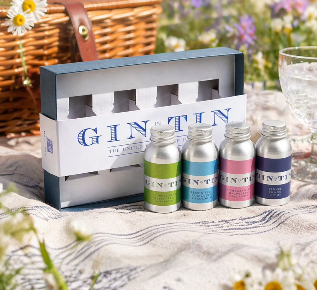 Set of mini gin tins with a branded box on a picnic blanket outdoors.