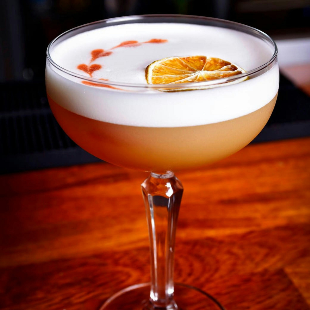 Cocktail with foam and an orange slice on a wooden surface