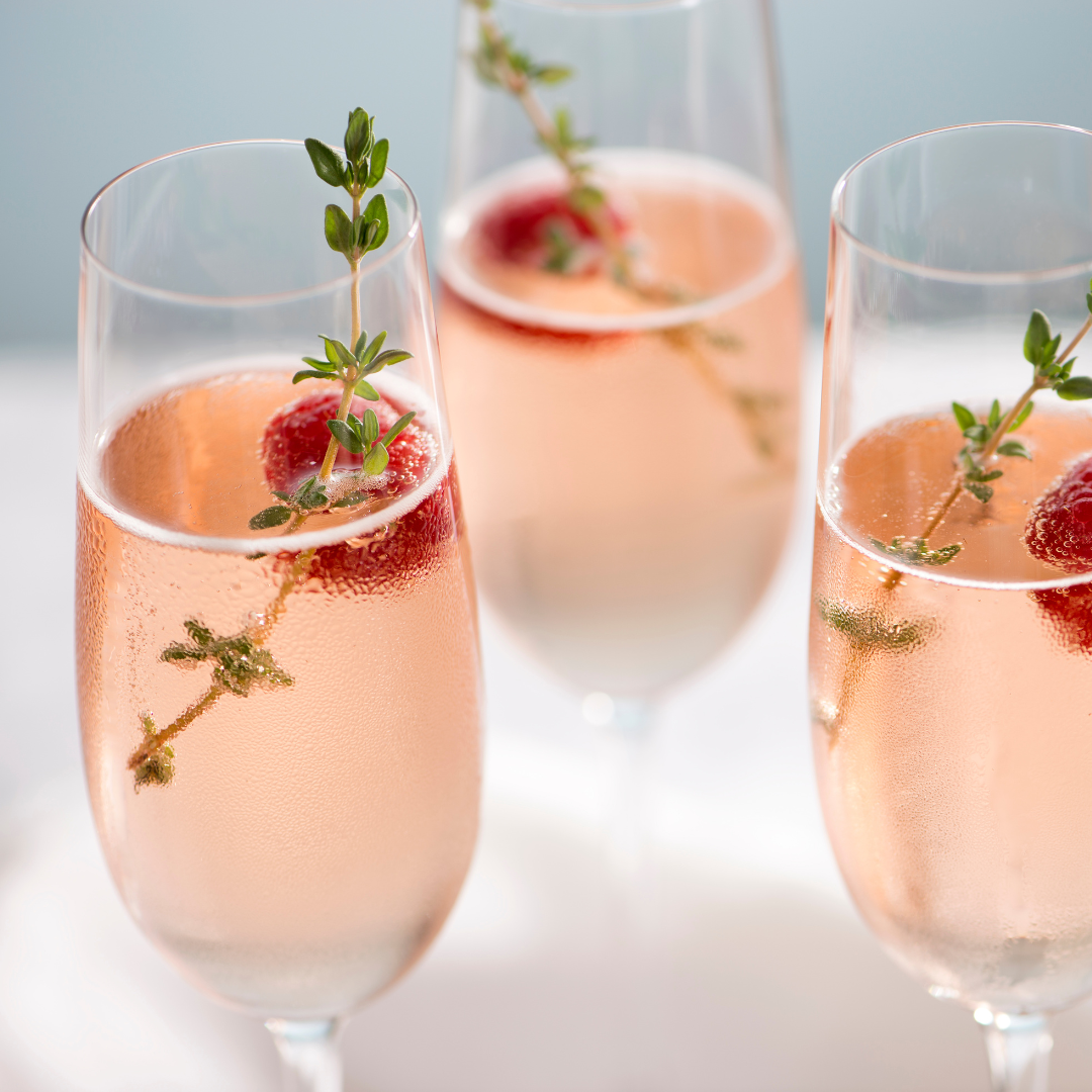 Rose Syrup G&Tee Time cocktail in a glass with ice, garnished with cucumber ribbon, fresh raspberries and mint leaves