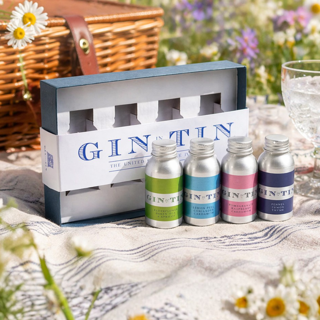 Set of mini gin tins with a branded box on a picnic blanket outdoors.