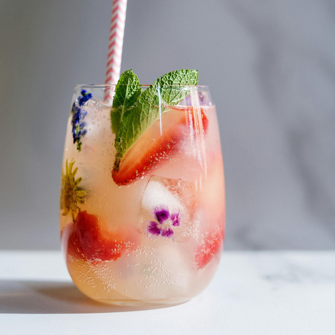 Blooming Delicious Gin Fizz in a highball glass over ice, garnished with strawberries and edible flowers”
