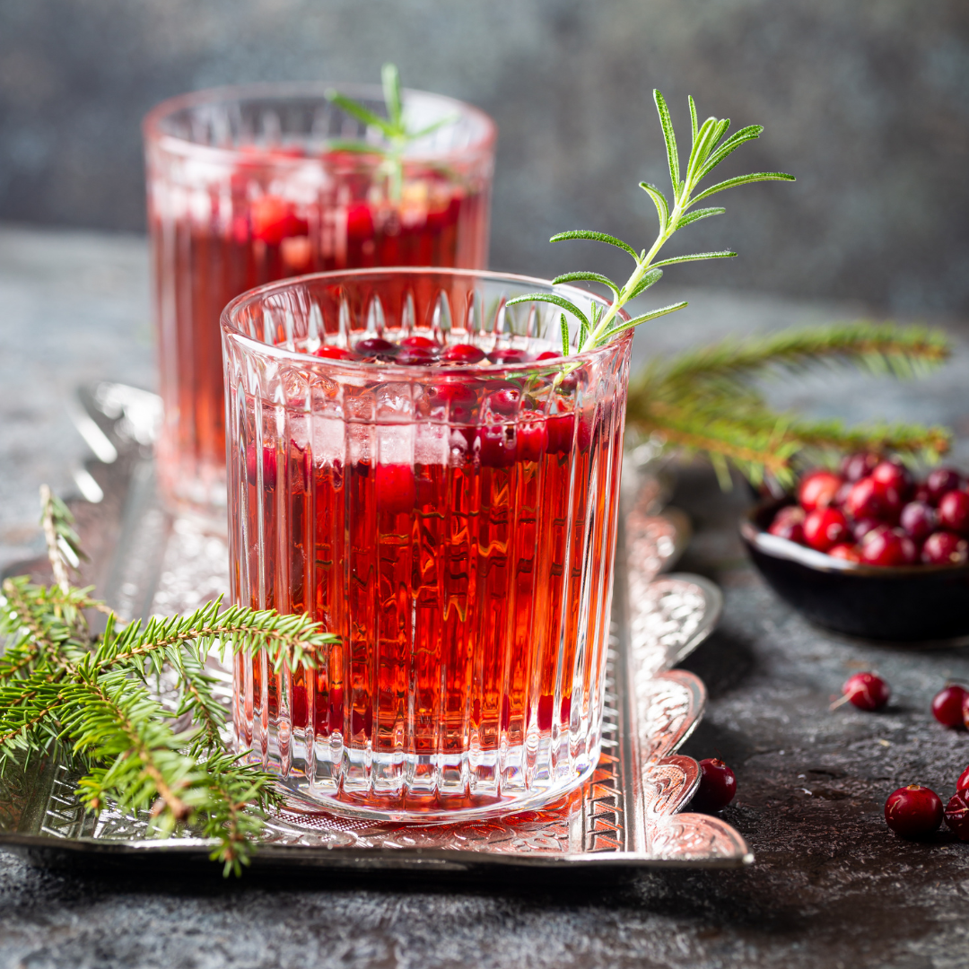 Two glasses of red cranberry cocktail with rosemary garnish on a dark surface.
